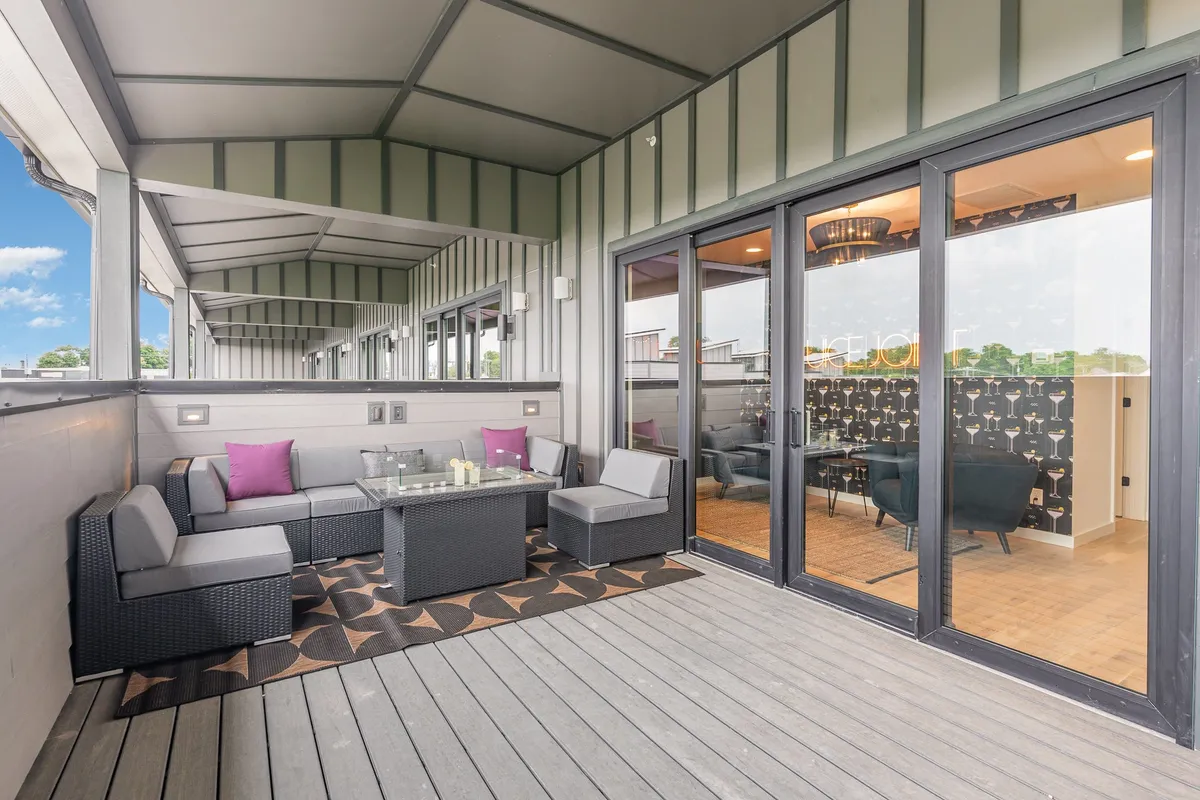 An elegantly arranged outdoor seating area featuring a coffee table and stylish, colorful cushions. The scene is set outdoors, with the gentle light of sunset visible, evoking a relaxed and celebratory mood. The arrangement clearly supports group gatherings and socializing, hinting at memorable evenings spent outdoors.